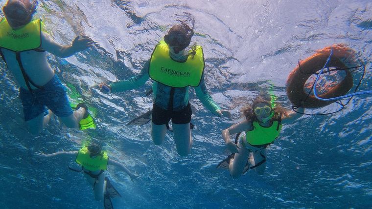 Snorkelers in yellow vests, one holding a safety ring, swimming together at Buck Island
