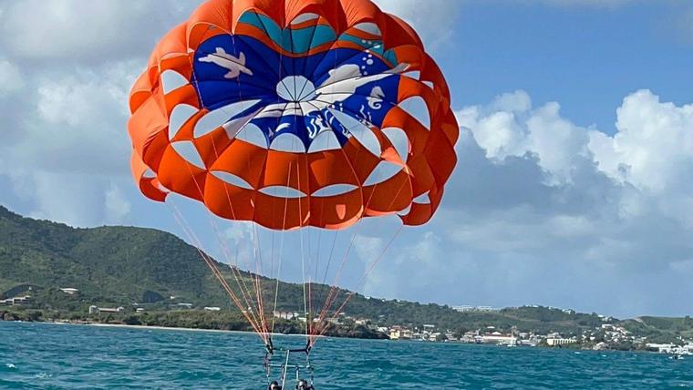 Parasail boat with an orange parachute flying behind it over blue water in St. Croix