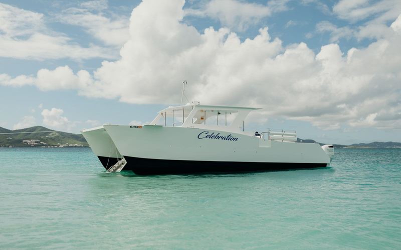 Celebration power catamaran anchored in shallow turquoise water off a beach