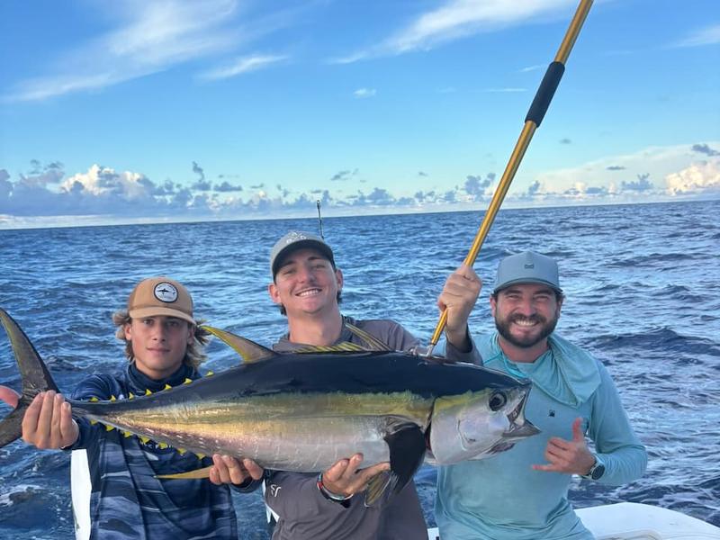 A smiling group on a fishing charter holding up a wahoo