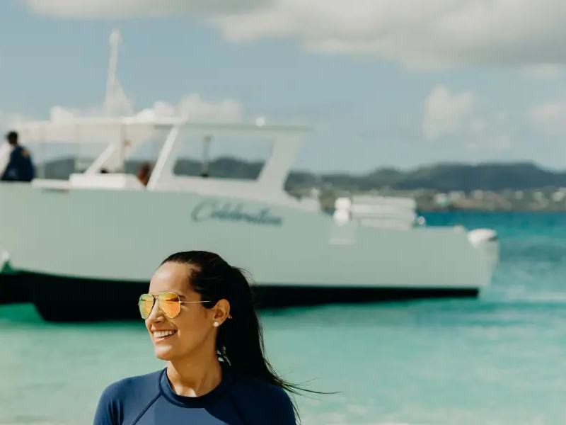 A crew member smiling in the shallows at Buck Island with Celebration anchored behind