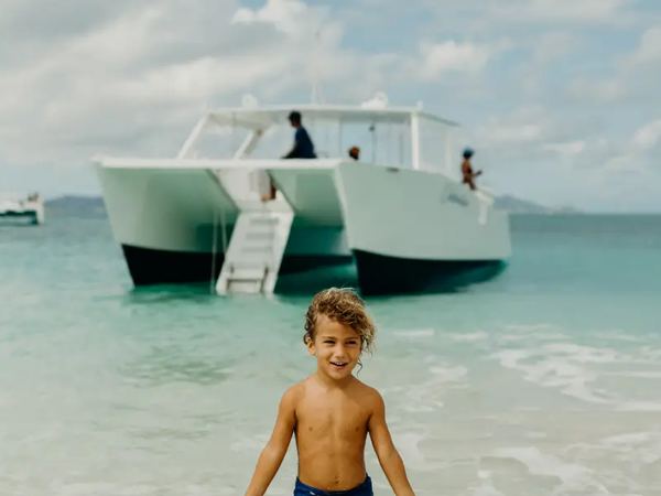 A young boy on the Turtle Beach sand with the Celebration catamaran anchored behind