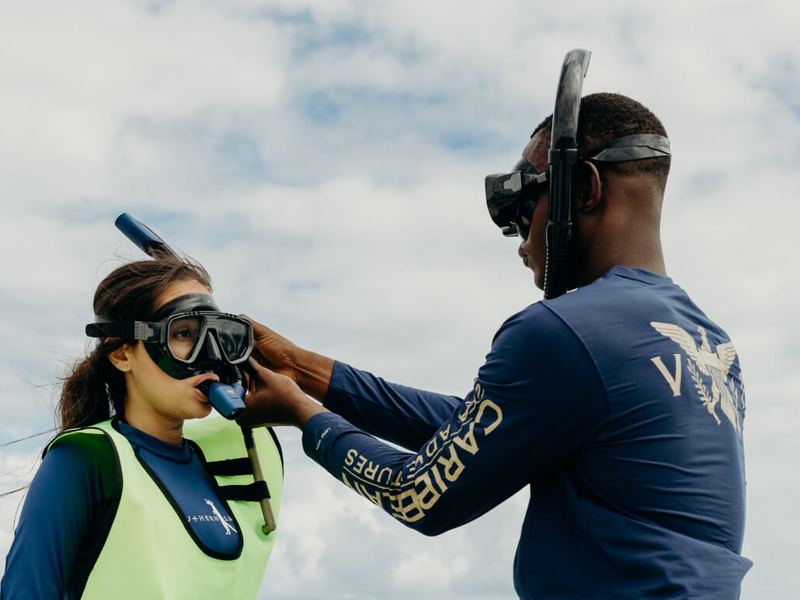 A crew member fitting a snorkel mask on a guest before her Buck Island snorkel lesson