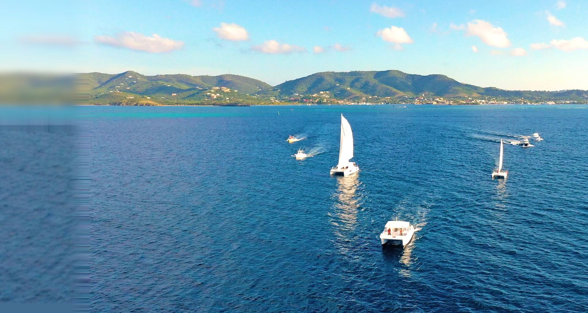 Caribbean Sea Adventures fleet of catamarans under sail and power heading out on deep blue water off St. Croix