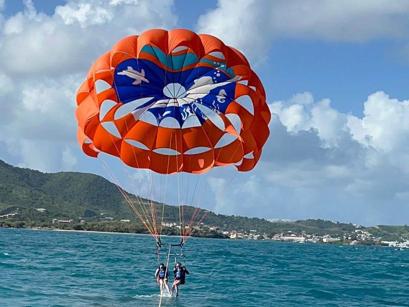 An orange parachute towing parasailers over turquoise water off the St. Croix coast
