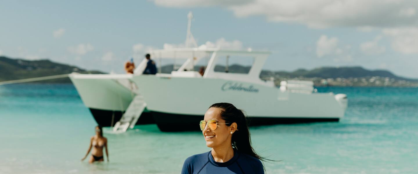 A guest smiling in the shallows with the Celebration power catamaran anchored behind