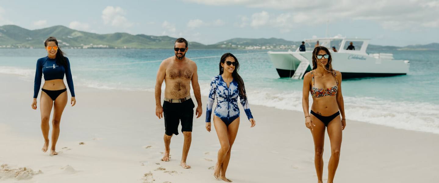 A private group walking on a Buck Island beach with the Celebration catamaran anchored behind