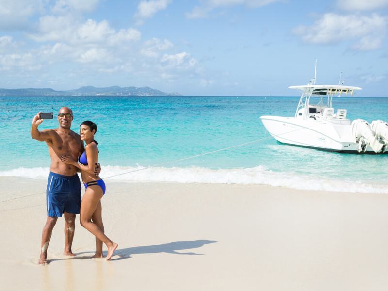 Guests on a white-sand beach with the Smooth Recovery center console anchored behind