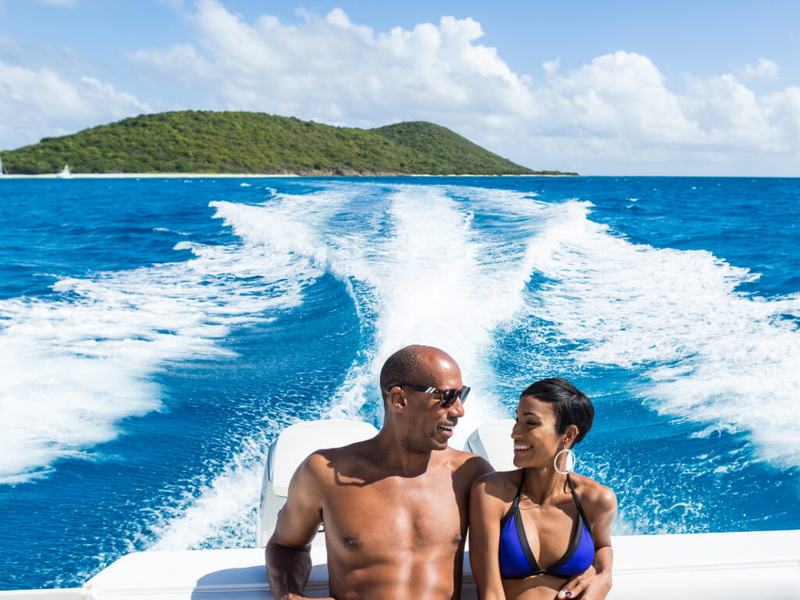 A couple on the stern of Smooth Recovery with the boat&rsquo;s white wake behind