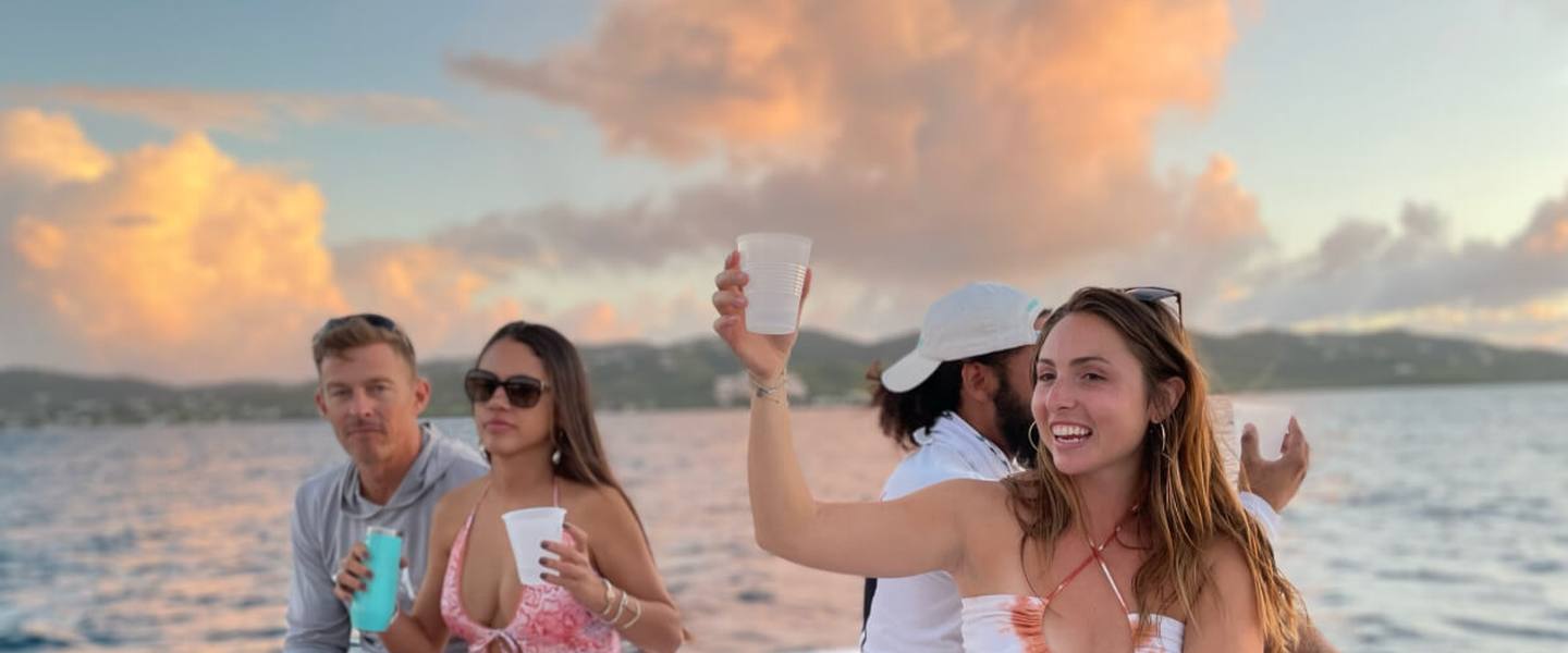 Friends raising their drinks on the bow of Celebration at sunset off St. Croix