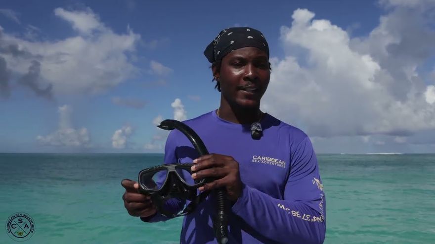 Captain Key of Caribbean Sea Adventures holding a snorkel mask, with turquoise water behind him